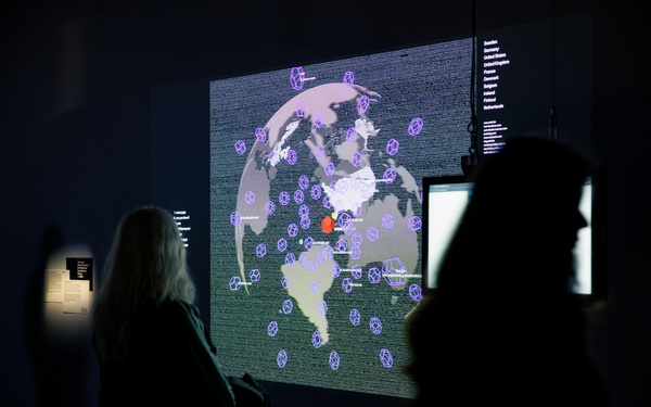 A person in a dark room looks at a screen on which an abstract globe and other data are displayed.
