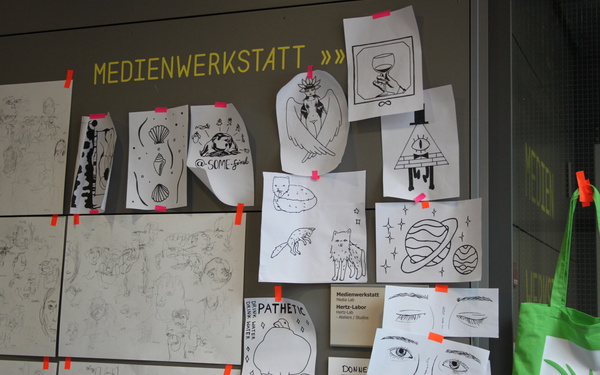 Mehrere Zeichnungen hängen an einer grauen Wand.
