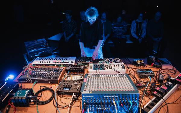 Zu sehen ist eine Person, die ein elektronisches Live-Set mit analogen und modularen Synthesizern durchführt.