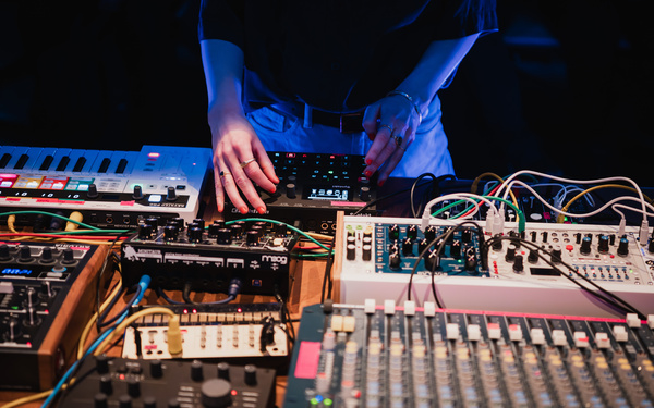 Zu sehen ist ein Tisch mit analogen und modularen Synthesizern, die von einer Person benutzt werden. 