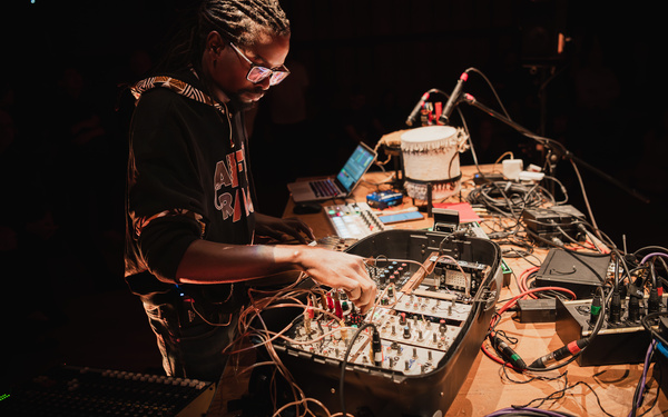 Zu sehen ist eine Person, die ein Konzert mit selbstgebauten Synthesizern und akustischer Percussion gibt. 