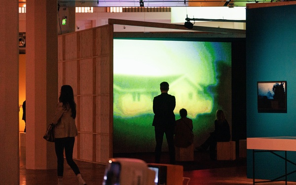 People can be seen looking at a large-format video projection.