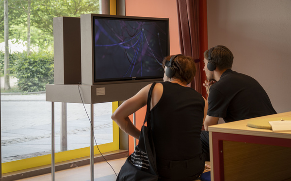 Two people can be seen sitting in front of a screen.