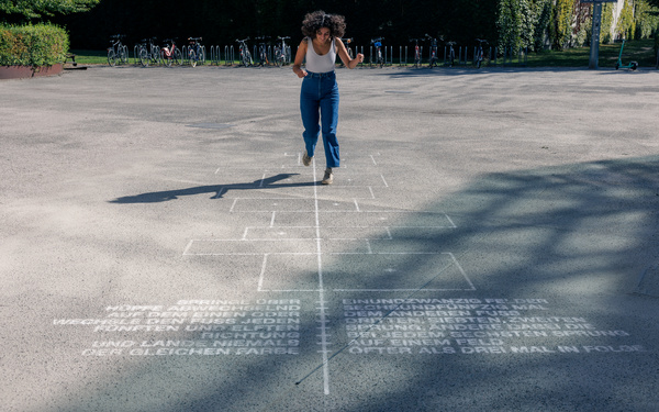 Eine Person hüpft draußen auf einem aufgemalten Spielfeld auf dem Asphalt.