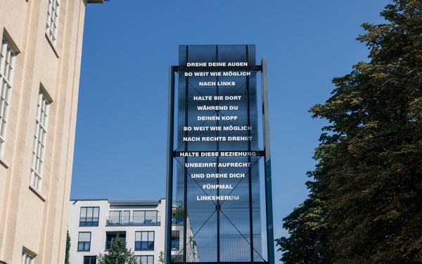 Zu sehen ist eine Stehle mit Schrift vor blauem Himmel.