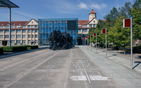 Zu sehen ist ein Gebäude und asphaltiertem Boden, der mit einem Himmel-Hölle-Spiel bemalt ist.