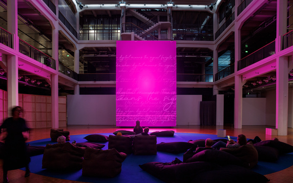 The scene shows a large screen with several people sitting on beanbag chairs in front of it. 