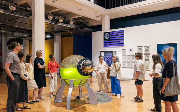 A guided tour group standing in front of a glass sphere filled with green liquid.