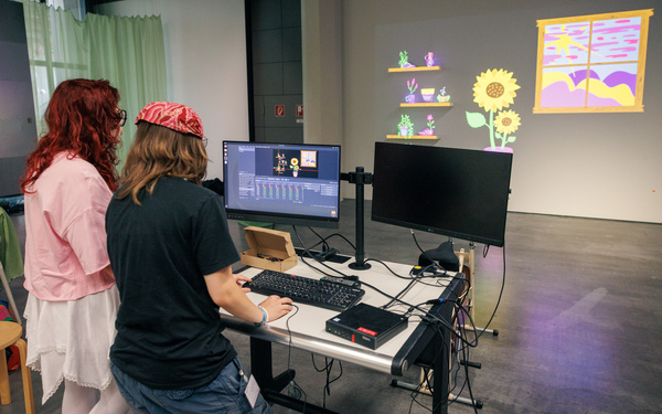 Das Bild zeigt zwei Personen, die vor einem Computer stehen und eine Projektion betrachten.