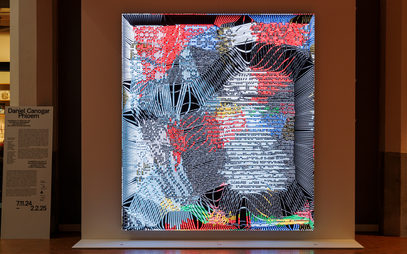 Zu sehen ist eine Installation mit einem großen Bildschirm, der viele Linien zeigt.  