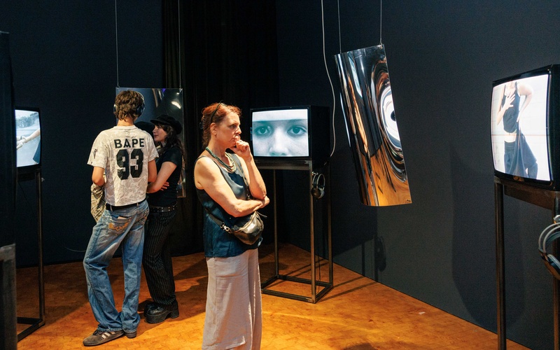 Zu sehen sind Personen, die Bildschirme in einem Ausstellungsraum betrachten. 