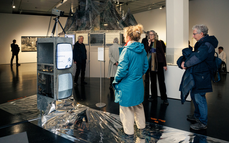 Eine Frau in blauer Jacke steht vor einem Röhrenmonitor.