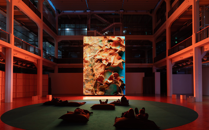 A group of people are sitting in front of a huge screen displaying an abstract artwork.