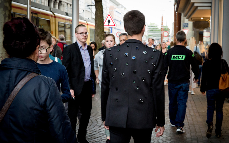 A Man wears a Jacket with some Camera-objectives in it