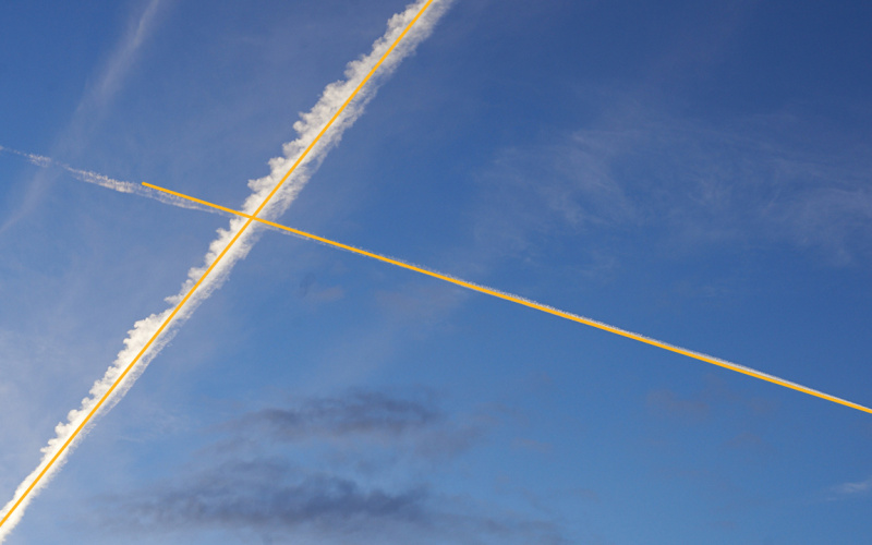 Foto des Himmels mit überkreuzten Kondensstreifen von Flugzeugen.