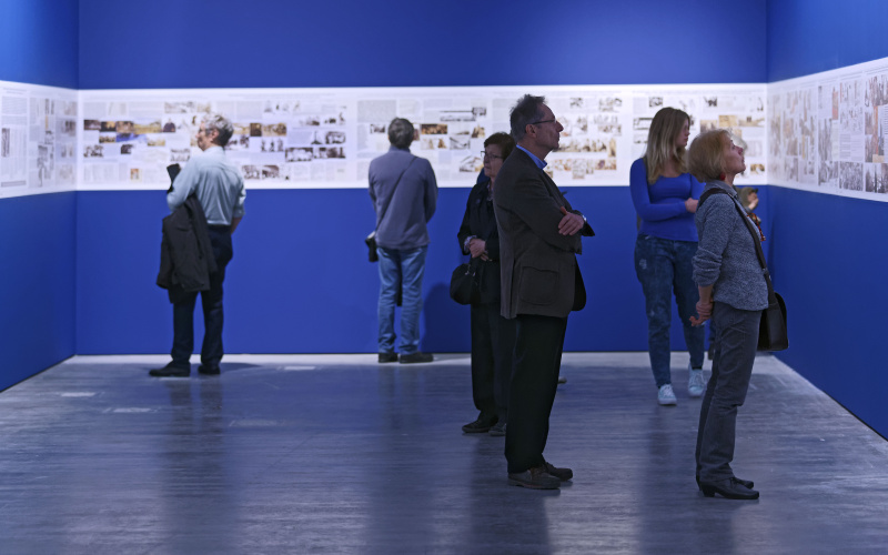  People looking at pictures of the exhibition, which are issued on a blue background