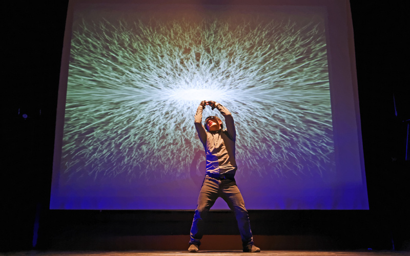 A man performs in front of a canvas on which a luminous ball can be seen