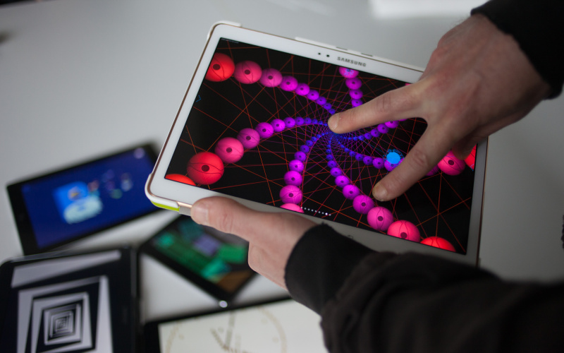 Nahaufnahme: Jemand bedient mit zwei Fingern eine künstlerische App auf einem Tablet. Im Hintergrund liegen weitere Tablets mit unterschiedlichen Apps.