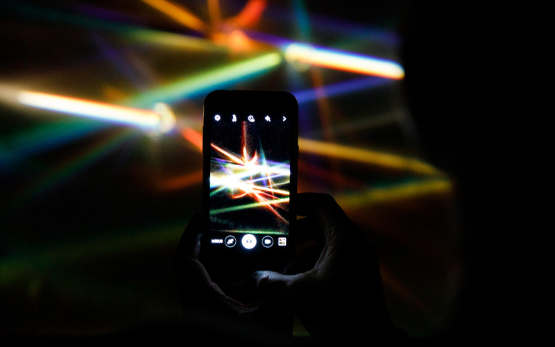A smartphone in camera mode photographs the beams of colorful light prisms.