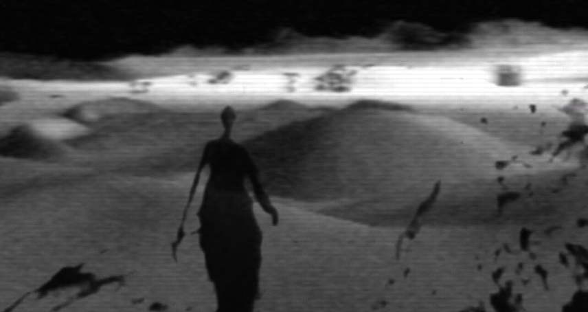 The picture is in black and white, a shady figure walks through the desert