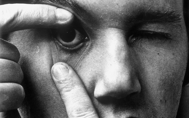 Die Portraitaufnahme zeigt Peter Weibel im Rahmen der Ausstellung »respektive Peter Weibel«. Auf dem Foto öffnet der Künstler sein rechtes Auge mit den Fingern.