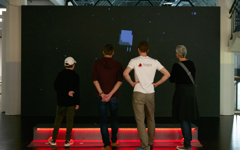 Vier Personen stehen vor der Installation des Computerspiels »Rakete«.