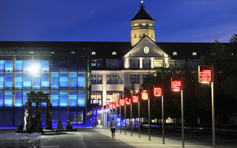 The ZKM at night: on the left of the cube in front of it the installation »Temple« and right of the road to the entrance with glowing red flags