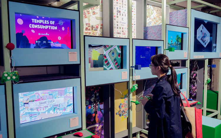 Person stands in front of several screens with a gaming controller