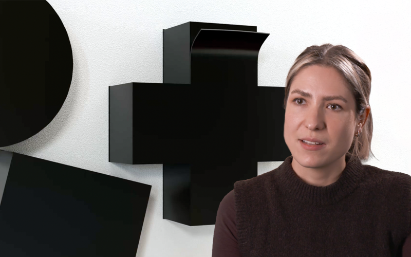 Ein Foto von Carolyn Kirschner vor einen weißen Hintergrund mit einem schwarzen Kreuz des Künstlers Malewitsch.