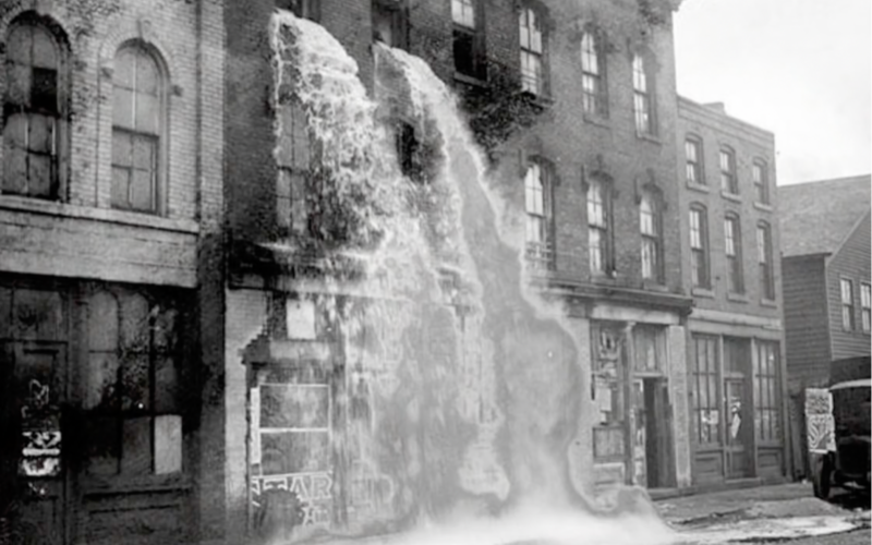 You see a factory building with a waterfall bursting out of the window in black and white.