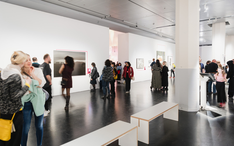 Zu sehen ist ein Ausstellungsraum in dem sich mehreren Personen Werke anschauen. 