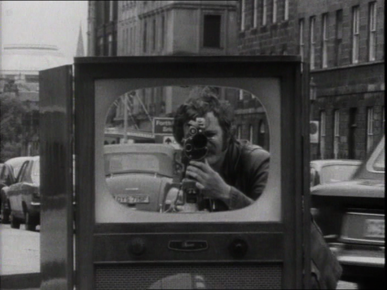 Zu sehen ist eine Schwarz-Weiß-Aufnahme, die einen Fernseher auf einer Straße zeigt.