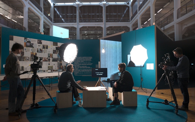 The video shows Johan Grimonprez and Max Clausen sitting across from each other while being filmed.